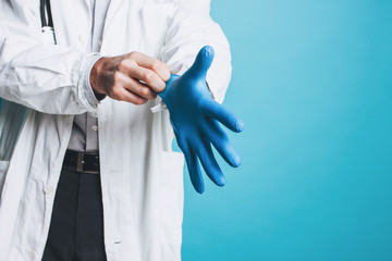 Crop photo of man doctor in white coat puts on rubber medical gloves  isolated on blue background