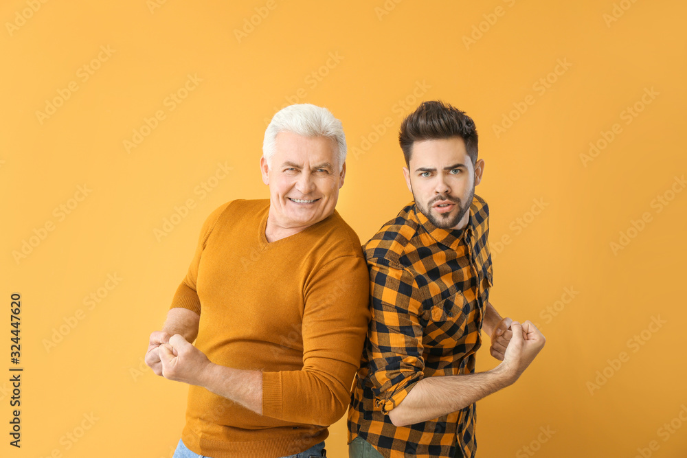 Wall mural Young man and his father showing biceps on color background