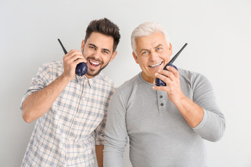 Young man and his father with walkie-talkie on light background