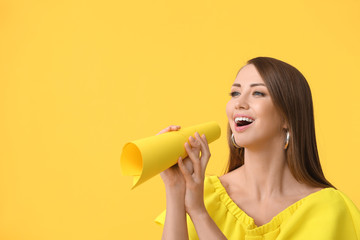 Young woman with paper megaphone on color background