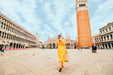 woman in elegance yellow sundress with straw bag walking by Venice saint marco square