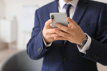 Young businessman with mobile phone in office, closeup