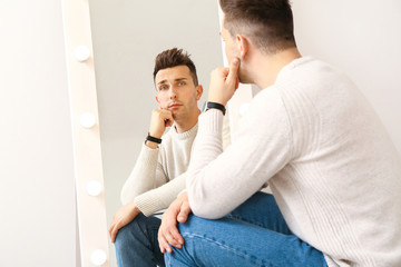 Thoughtful young man looking at his reflection in mirror