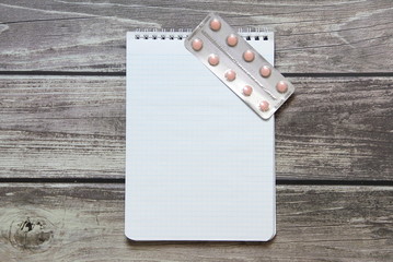 Notepad with a blank white sheet in a checker paper with pills in a blister lies on the background of wooden boards