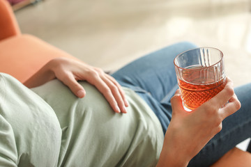 Young pregnant woman drinking alcohol at home