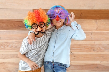 Little children in funny disguise on wooden background. April fools' day celebration