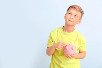 Thoughtful cute boy with piggy bank and money on white background