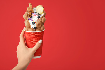 Female hand with delicious sweet bubble waffle on color background