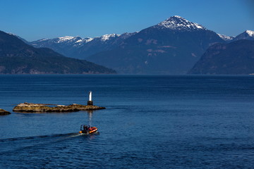 A motor boat carries tourists from Horseshoe Bay to observe whales in the Strait of George,  blue water in a bay against a mountain range and clear blue sky