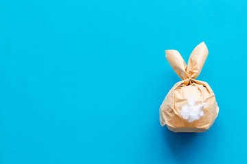 Easter gift in shape of bunny with tail on blue background top-down copy space