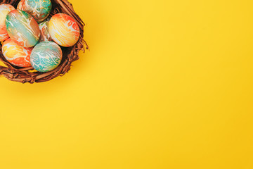 Coloeful easter eggs in nest on yellow color background. Space for text.