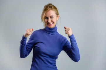 Happy smiling blonde woman in a blue sweater on a blue background shows the joy of good luck