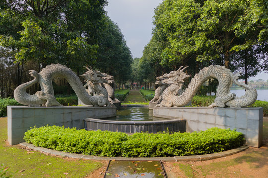 Four dragon statues in a public park with big fountain and green alley 