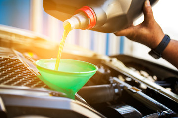 Car mechanic replacing and pouring fresh oil into engine..