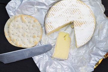 Camembert cheese whole with slice next to water crackers and knife - overhead image