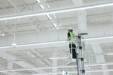 Unidentified male worker operating maintenance of warehouse lighting system