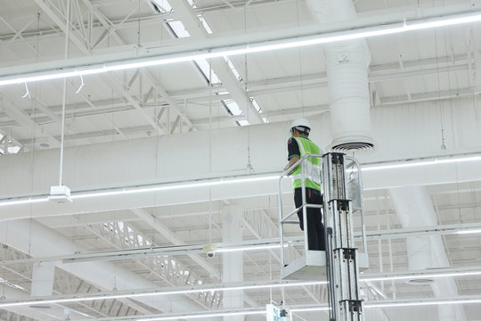 Unidentified male worker operating maintenance of warehouse lighting system