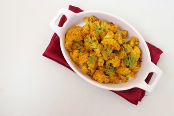 Dry cauliflower curry or Gobhi ki sabji or Gobi Masala served in white bowl with wooden spoons and coriander over white background with copy space.