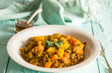 Lentil and vegetable curry in bowl on rustic blue table with chutney in background - selective focus image