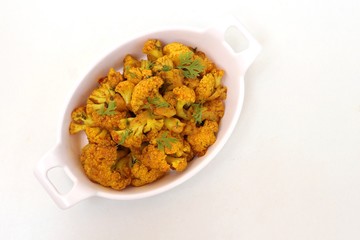 Dry cauliflower curry or Gobhi ki sabji or Gobi Masala served in white bowl with wooden spoons and coriander over white background with copy space.