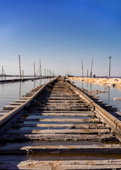 old rails go into the distance in the water against a blue sky. Nature destroys what man has built....