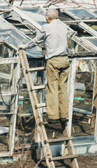 Fototapeta na wymiar The old man on the stairs repairs the greenhouse