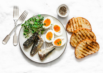 Grilled bread, sardines, boiled eggs, micro greens on a light background, top view. Delicious...