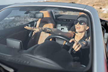 Portrait of a young woman driving a cabriolet near the ocean on a summer time. View through the...
