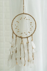Dream catcher with feather hanging on white fabric background
