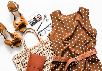Polka dot summer brown dress, suede wedge sandals, eco straw tote bag, cosmetics on a light background, top view. Women's clothing set