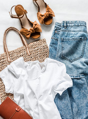 Women's clothing summer - mom's jeans, suede brown wedge sandals, white cotton t-shirt, eco bag straw on a light background, top view