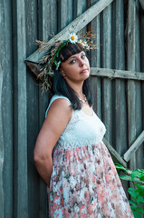 Portrait of a girl with a wreath of wild flowers on her head. Wooden fence.