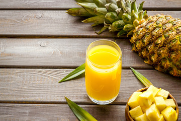 Pineapple juice in glass closeup near sliced fruit on wooden background copy space