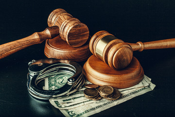 Bribe concept. Dollar banknotes, handcuffs and gavel on dark black table
