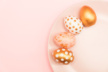 Top view of pink, white and golden decorated eeaster eggs on pink plate on pink background. Trendy holiday backdrop.