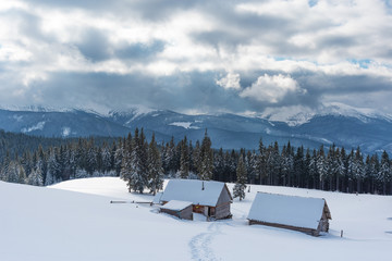 Charming snow-capped houses on a mountain Carpathian mountain valley, with magnificent views of peaks in winter.