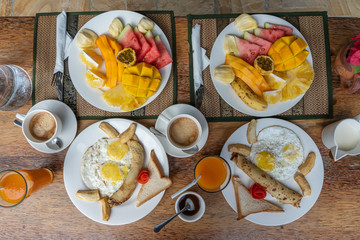 Tropical breakfast of fruit, coffee and scrambled eggs and banana pancake for two on the beach near sea. Top view, table setting.