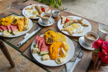 Tropical breakfast of fruit, coffee and scrambled eggs and banana pancake for two on the beach near sea