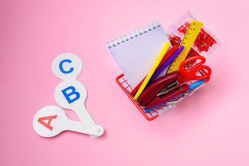 Back to school. Bright stationery items in a mini supermarket basket on a pink background.