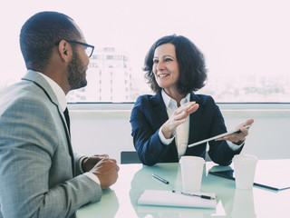 Joyful corporate trainer telling newcomer about work in company. Happy business woman holding...