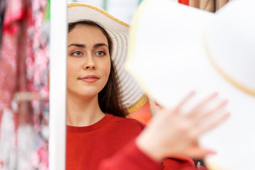 A pretty Caucasian woman tries on a straw hat in front of a mirror in a store. Rear view, face reflected in the mirror. Close up. Shopping concept