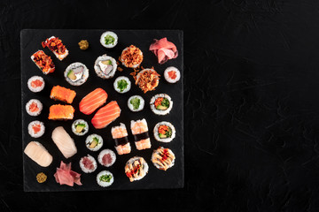 Large sushi set, shot from the top on a black background with a place for text. An assortment of various maki, nigiri and rolls