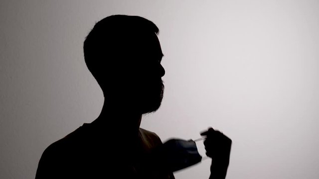 Silhouette of a Person Taking off Hygiene Face Mask to Prevent Spreading Disease
