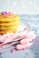 pancakes with pink topping on a white plate next to pink fluffy grass on a blue table