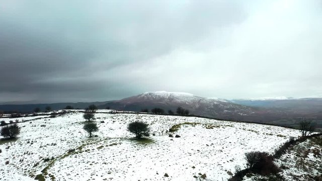 Aerial ascending over snow capped hill revealing mountain