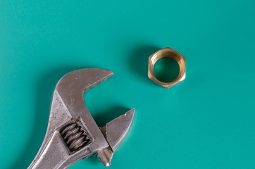 Adjustable wrench and one nut on a green background. Brass nut for pipe compression fittings. ...