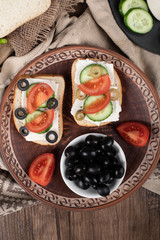Fototapeta na wymiar Tomato cucumber sandwiches with olives in a brown platter. Top view