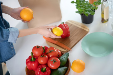 Citruses in female hands over a table with vegetables.