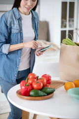 Young girl with a smartphone in hands near table with vegetables.