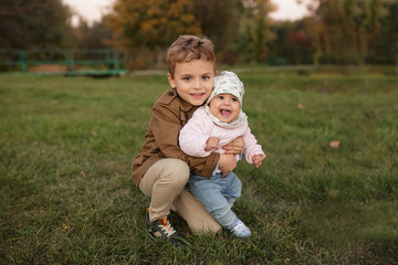 Fototapeta premium A little boy dressed in a brown coat smile and hug a his sister